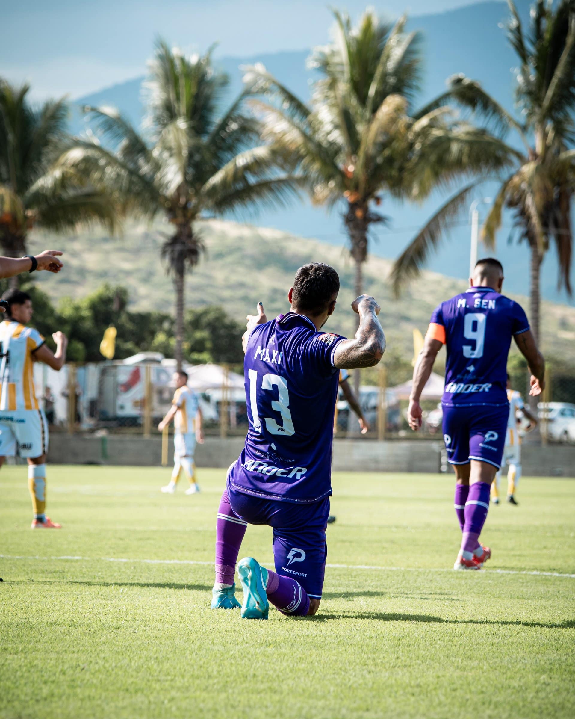 Maximiliano Pérez, número 13 de Comerciantes Unidos, de rodillas sobre el césped apuntando al cielo para celebrar su gol.